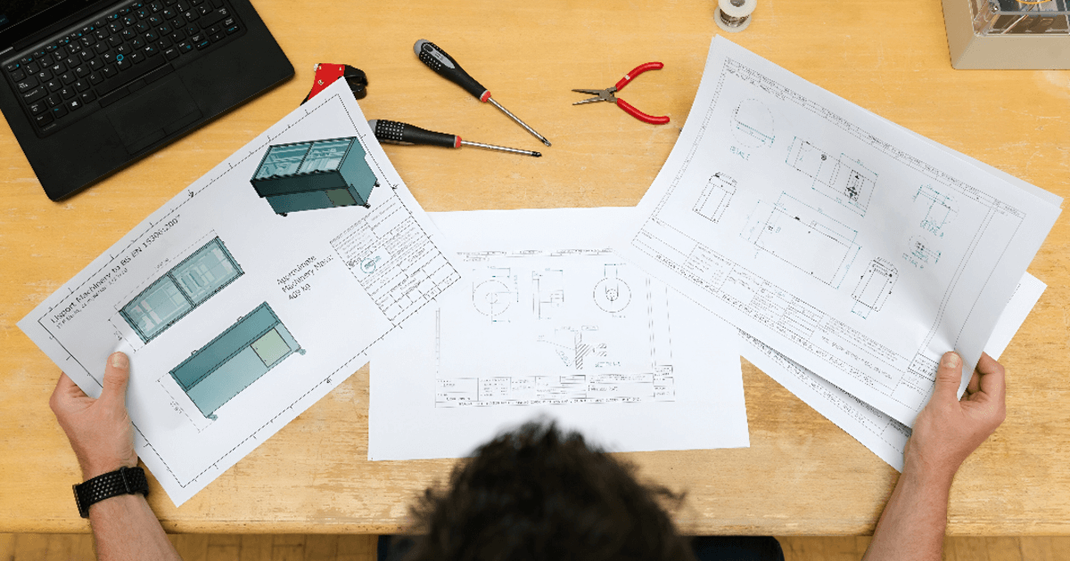A person reviewing 2D drafting plans on a wooden table.