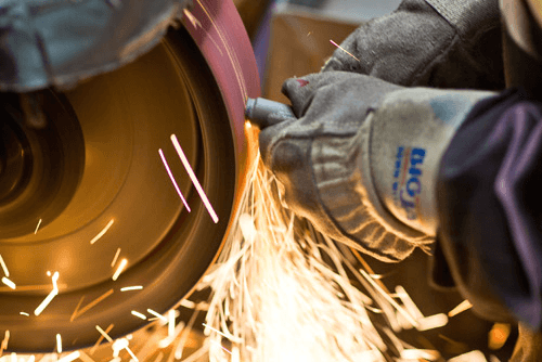 Close-up of hands performing finishing work on investment casting with sparks flying.