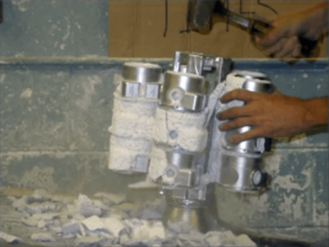 Worker performing investment casting knock out process.