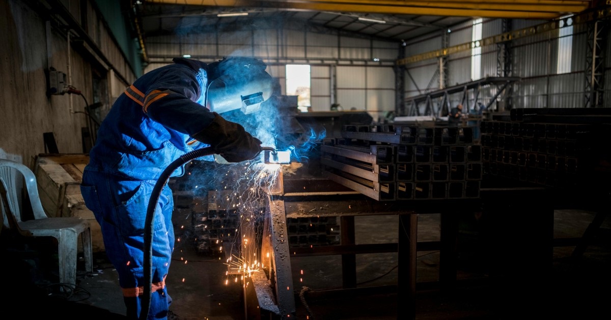  A man in a blue uniform welding steel, showcasing sheet metal fabrication services in action.